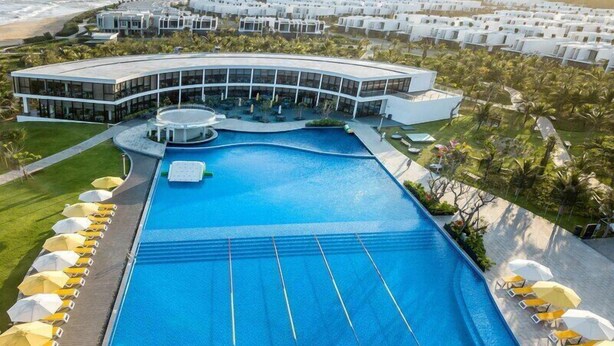 A large swimming pool with multiple lanes, surrounded by sun loungers and umbrellas, with a modern resort building in the background. - Viva Villa Oceanami (Nam Nha Trang)