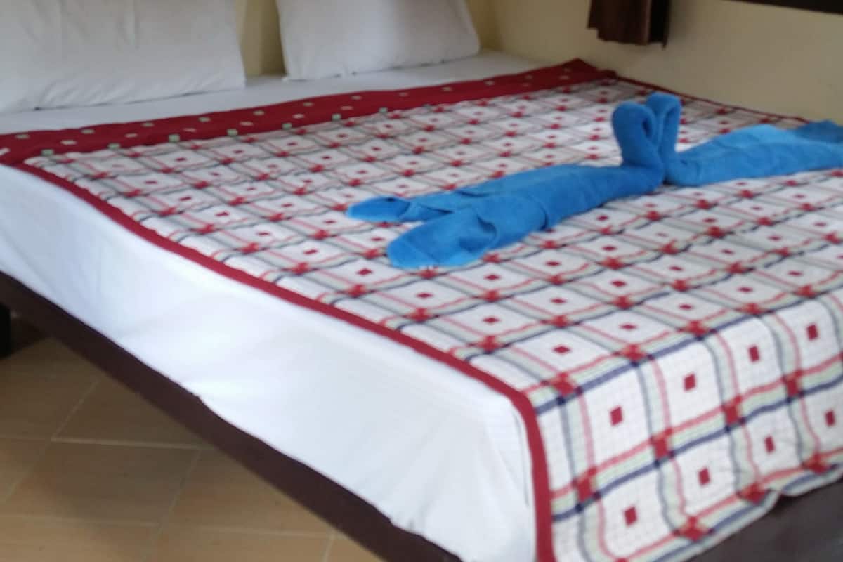 Een hotelkamer met een bed, witte kussens, een rood-wit gestreepte deken en een raam met gordijnen.