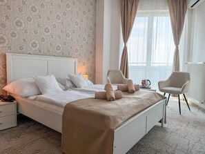 A neatly made bed with pillows and a blanket, a bedside table with a lamp, two chairs, and a window with curtains. - Hotel Modena (Bratislava)