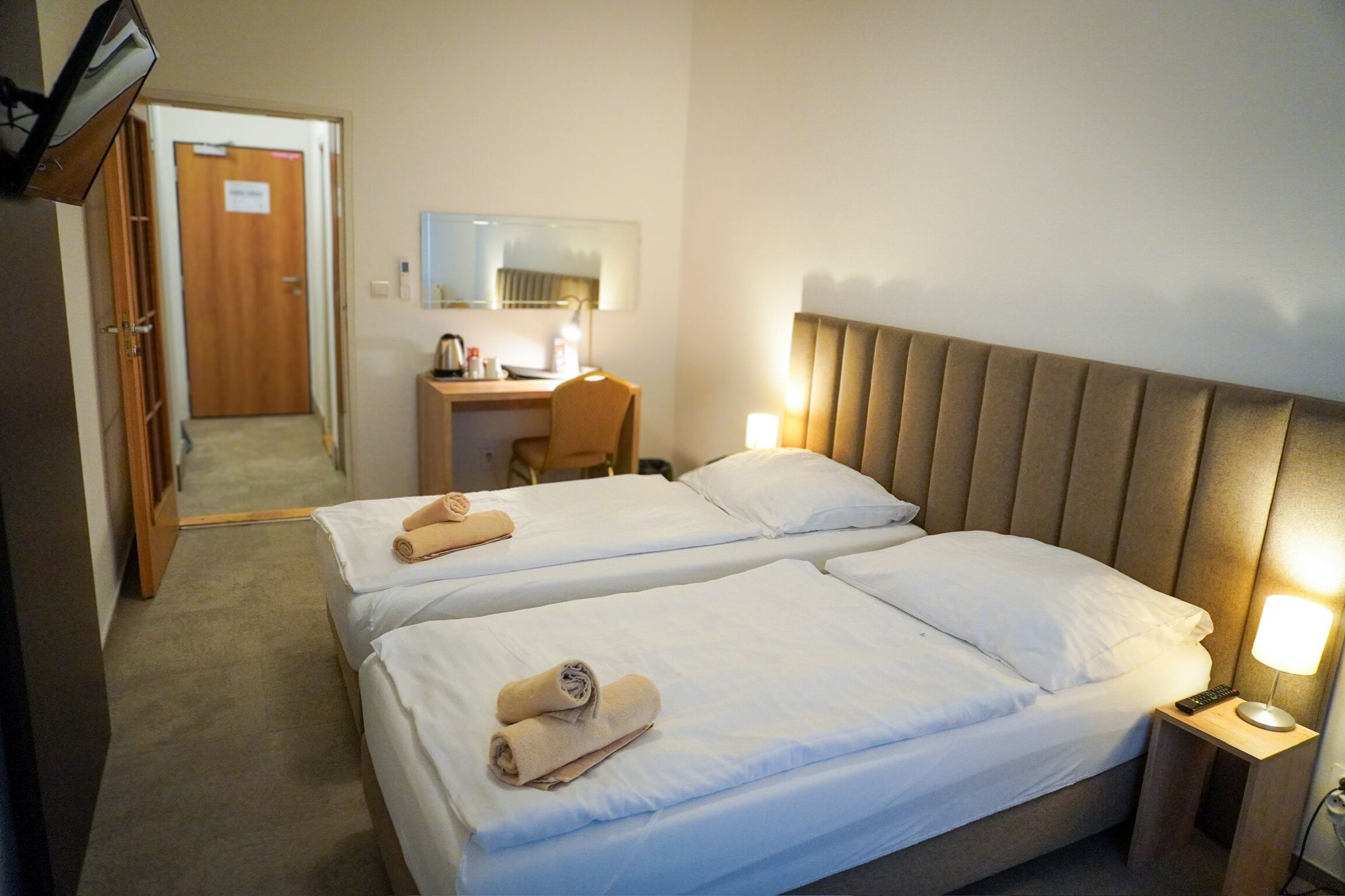 Une chambre d’hôtel avec deux lits, un bureau, une chaise, une lampe et une armoire.