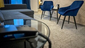 A modern hotel room with a grey sofa, two blue armchairs, a glass coffee table, and a patterned carpet. - Hotel Modena (Bratislava)