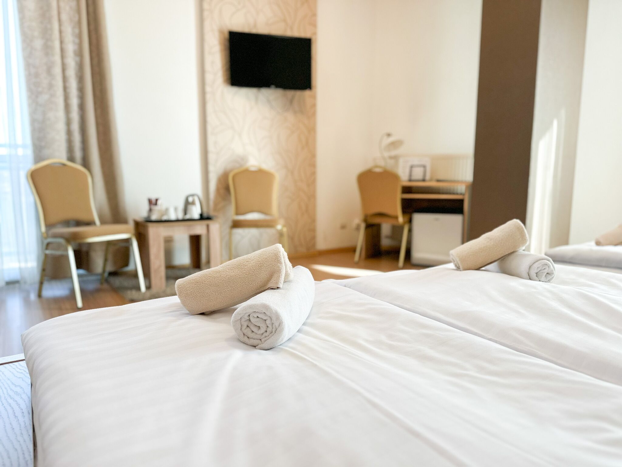 Une chambre d’hôtel avec deux lits, chacun agrémenté d’une serviette blanche soigneusement pliée. On y trouve deux chaises et une petite table avec une bouilloire. Un téléviseur est fixé au mur.