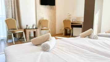 Une chambre d’hôtel avec deux lits, chacun agrémenté d’une serviette blanche soigneusement pliée. On y trouve deux chaises et une petite table avec une bouilloire. Un téléviseur est fixé au mur.