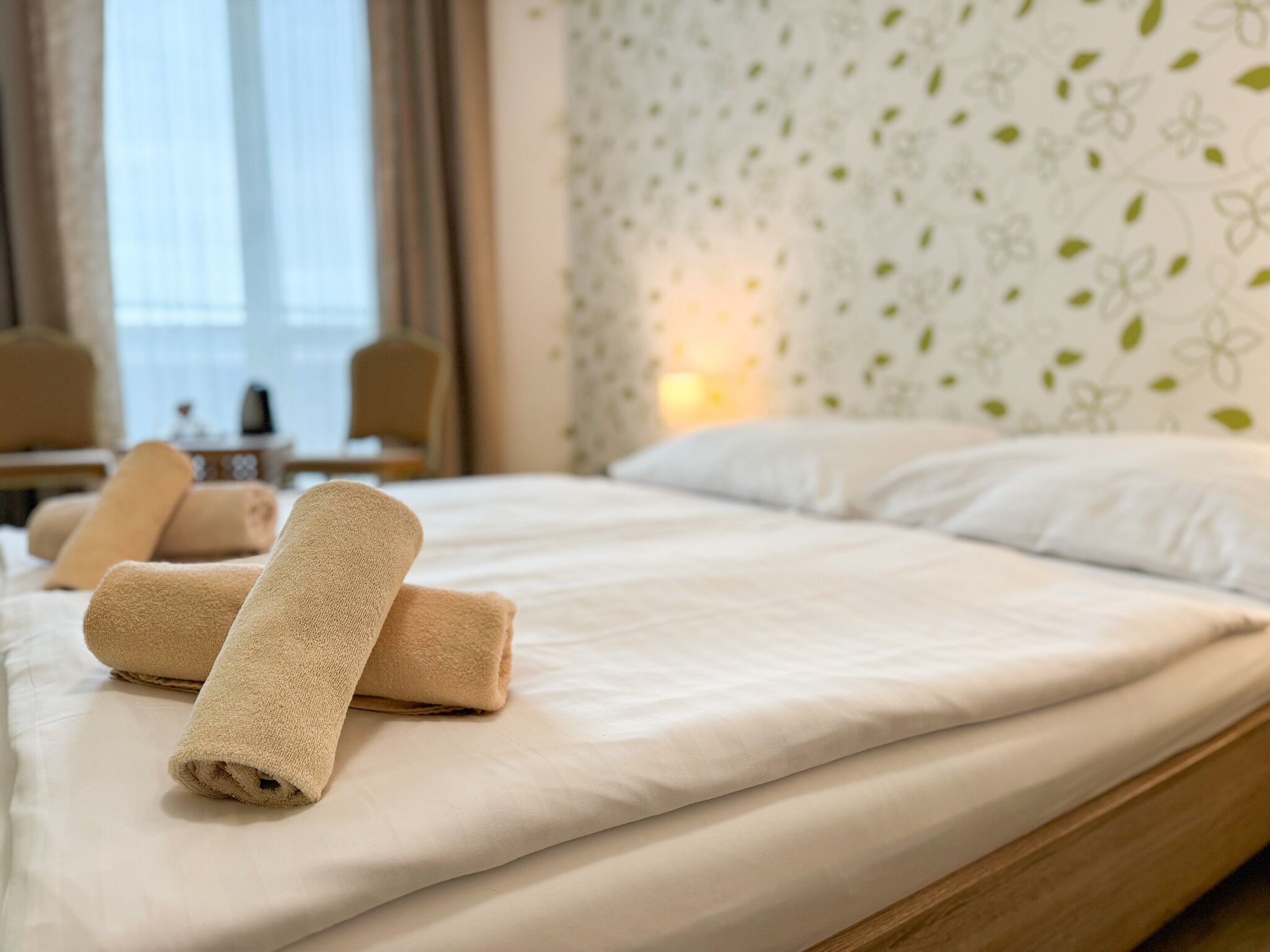 Een net opgemaakt bed met opgerolde handdoeken, een houten hoofdbord en een bloemen behang.