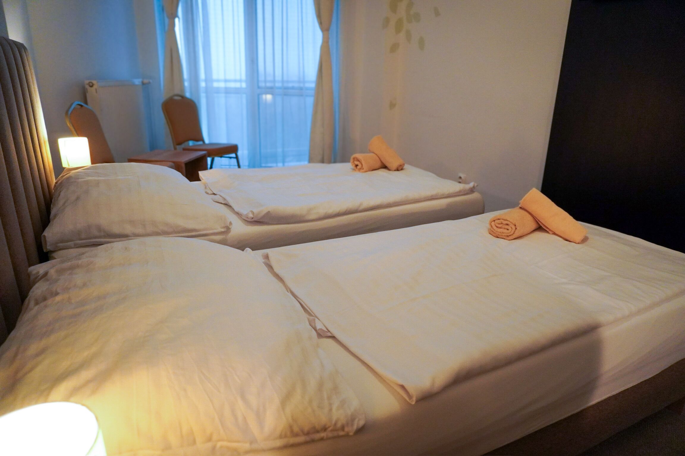 Ein Hotelzimmer mit zwei Betten, einem Sessel, einem Schreibtisch und einem Fenster mit Vorhängen.