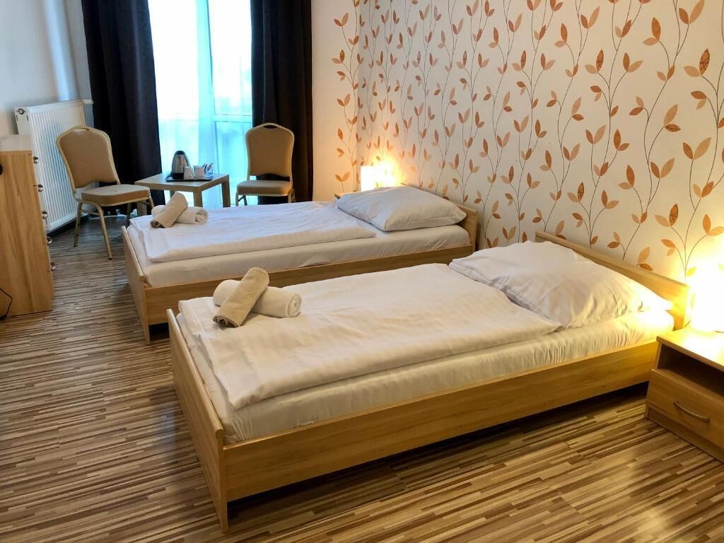 Habitación de hotel con dos camas individuales, una mesita con una silla, un radiador y una ventana con cortinas.