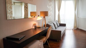 A modern hotel room with a desk, chair, and sofa. There is a large mirror above the desk and a window with curtains. - Hotel Modena (Bratislava)