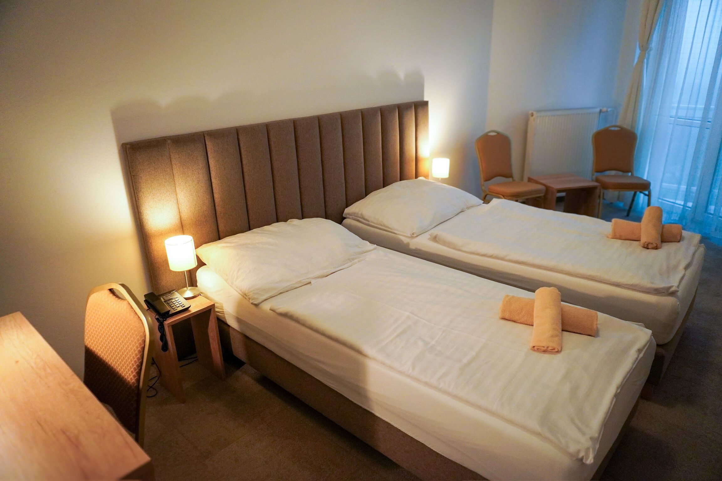 Quarto de hotel com duas camas, uma escrivaninha com telefone e uma cadeira.
