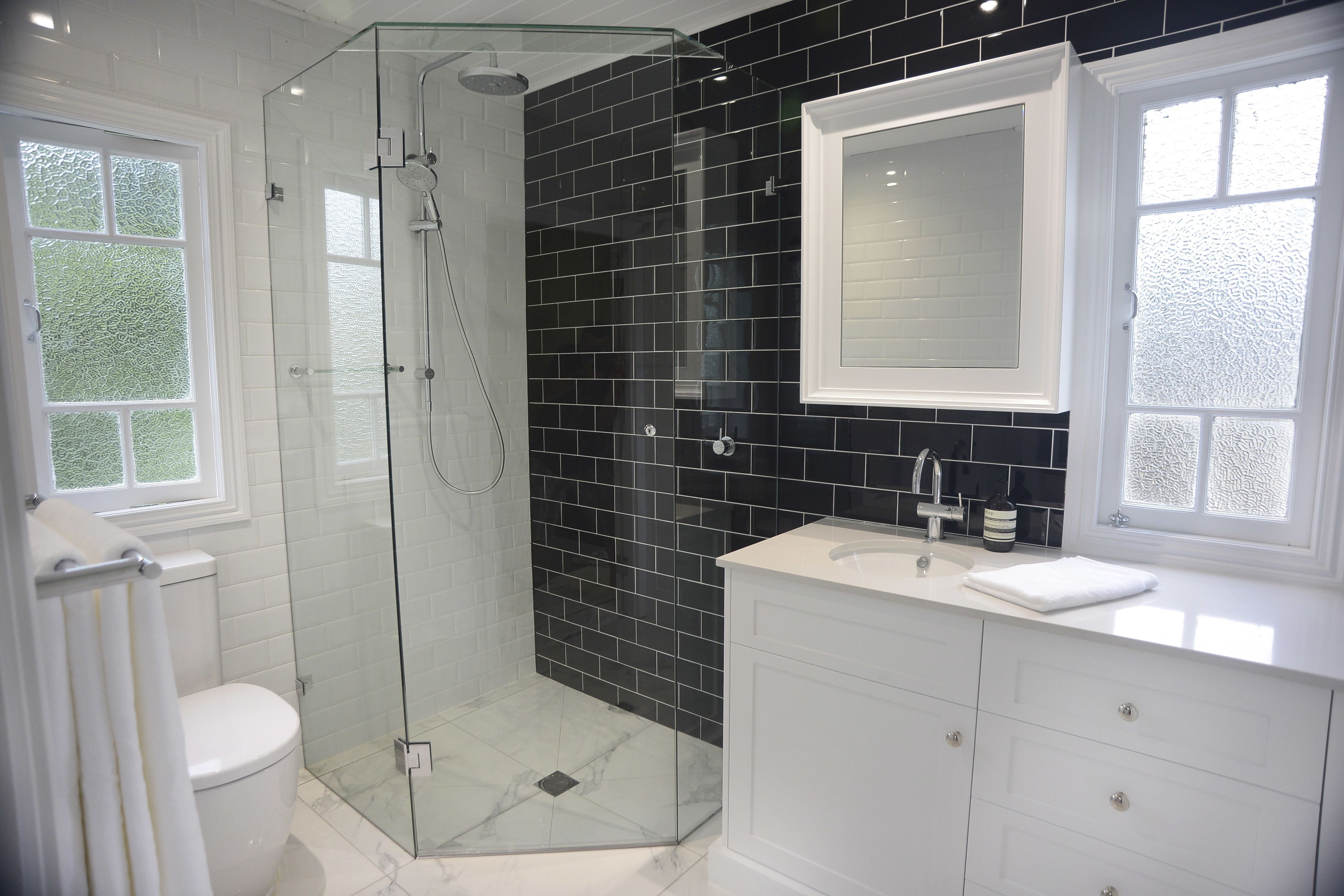 A modern bathroom with a glass-enclosed shower, white fixtures, and black tiled walls.