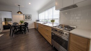 Una cocina moderna con comedor, que cuenta con un amplio ventanal, electrodomésticos de acero inoxidable y armarios de madera.