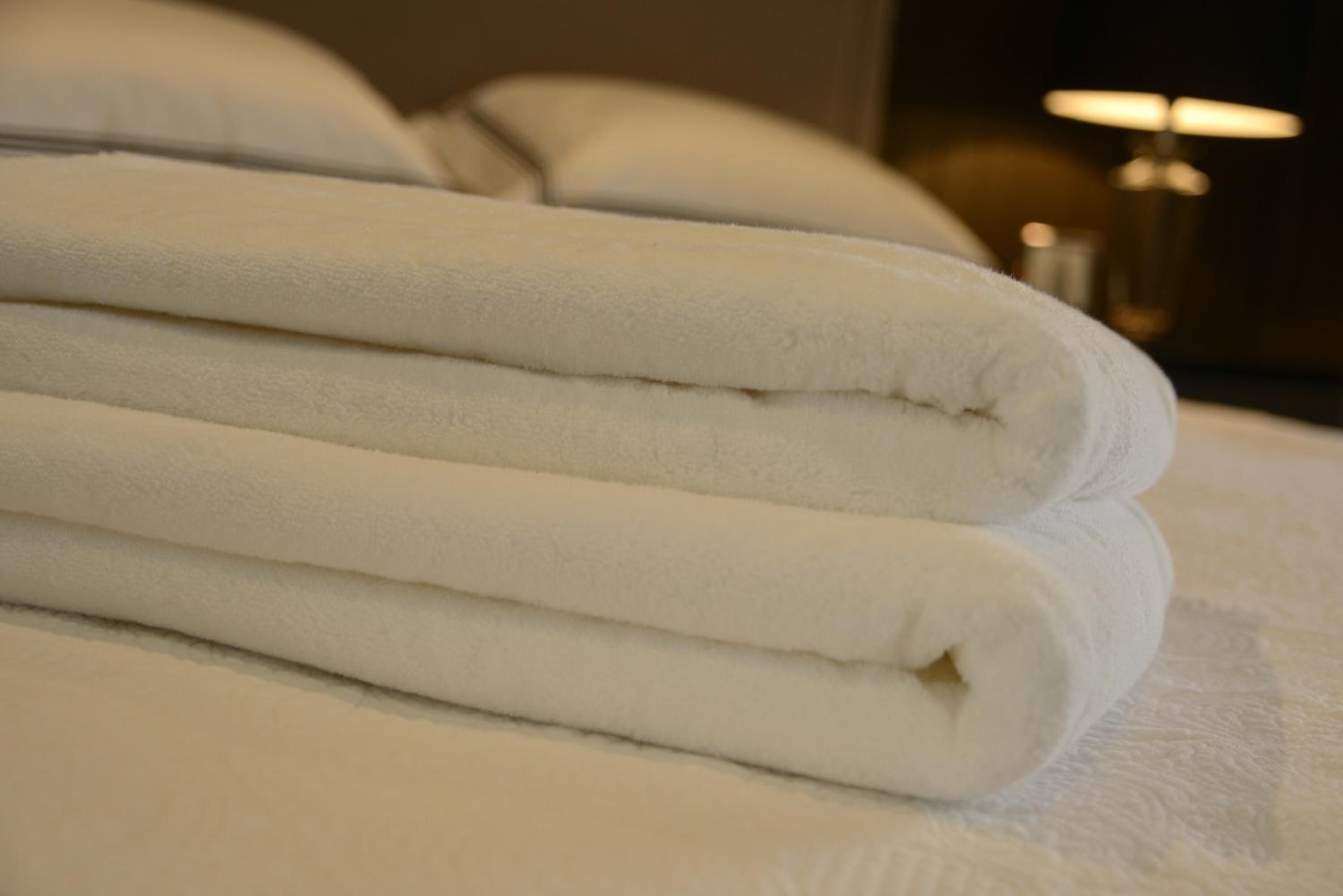 Una toalla blanca doblada cuidadosamente apilada sobre una cama con una colcha texturizada blanca.
