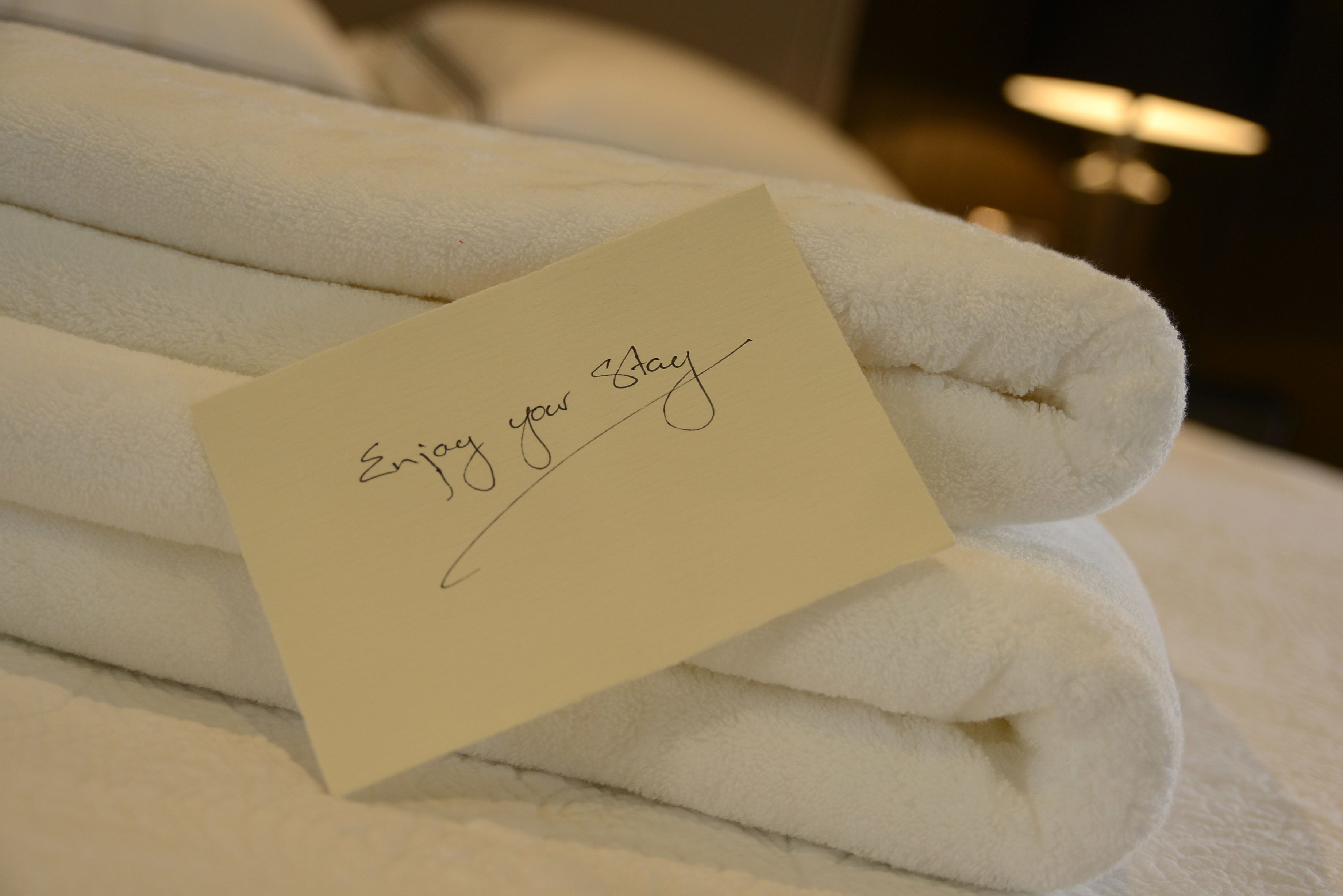 A stack of white towels with a note on top that says "Enjoy your stay".
