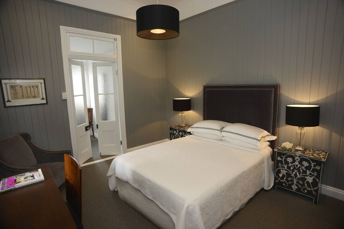 A neatly arranged bedroom with a bed, two bedside tables with lamps, a chair, and a door.
