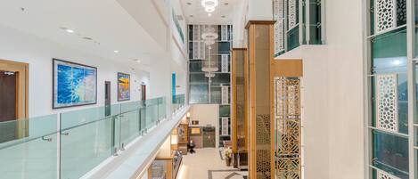 A spacious hotel lobby with a glass railing, artwork on the walls, and a decorative wooden partition.