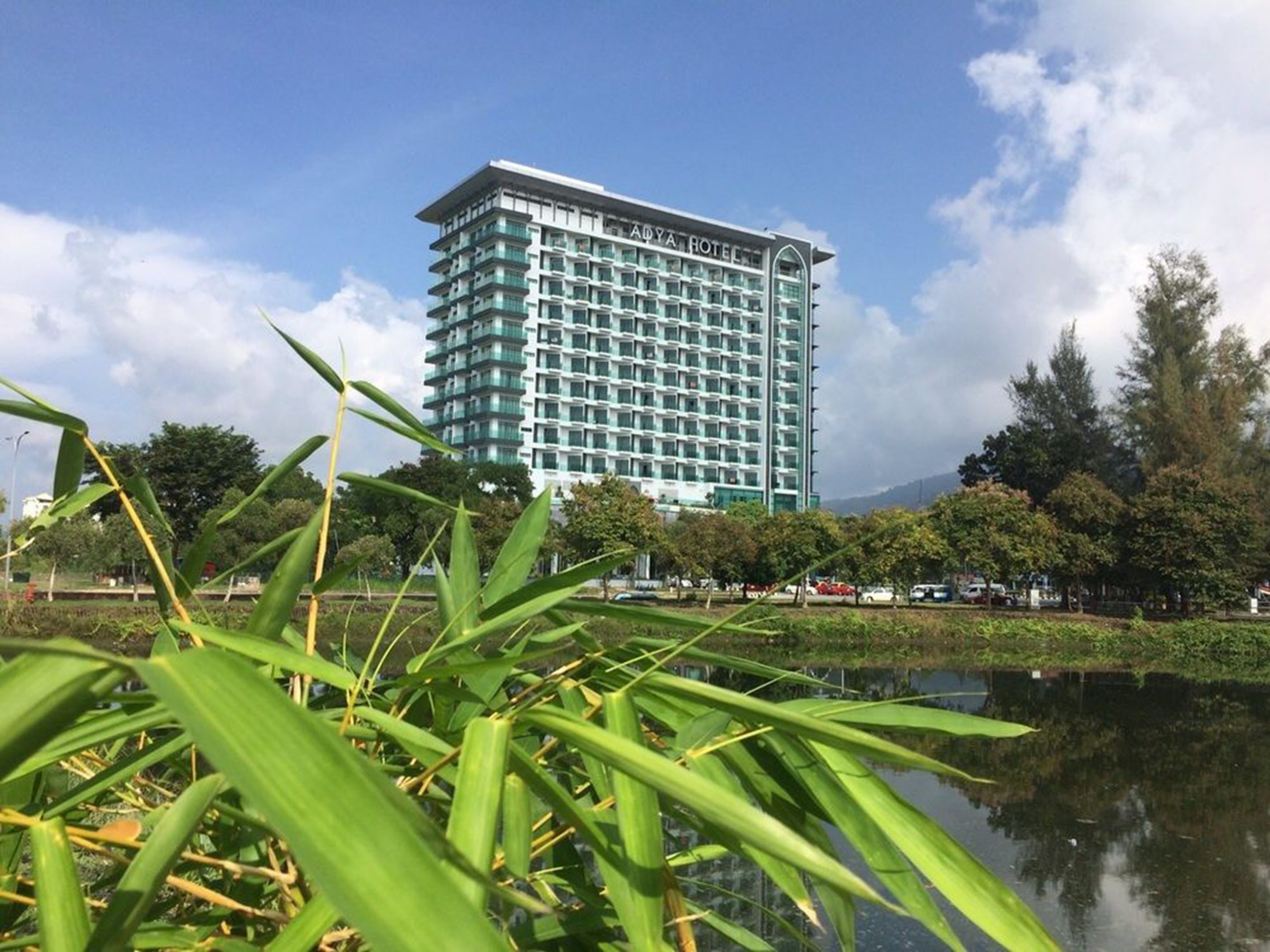 A high-rise hotel with multiple floors, surrounded by greenery and a body of water.