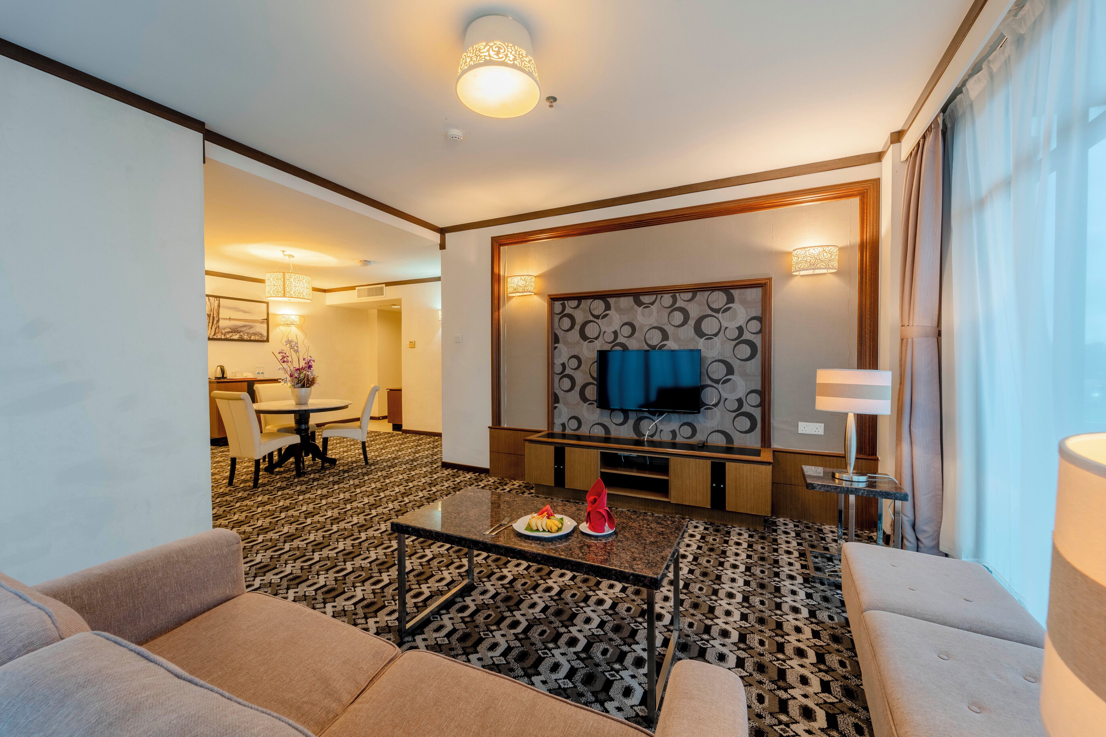 Une chambre d’hôtel avec un canapé, un coin repas, une télévision et une moquette à motifs.