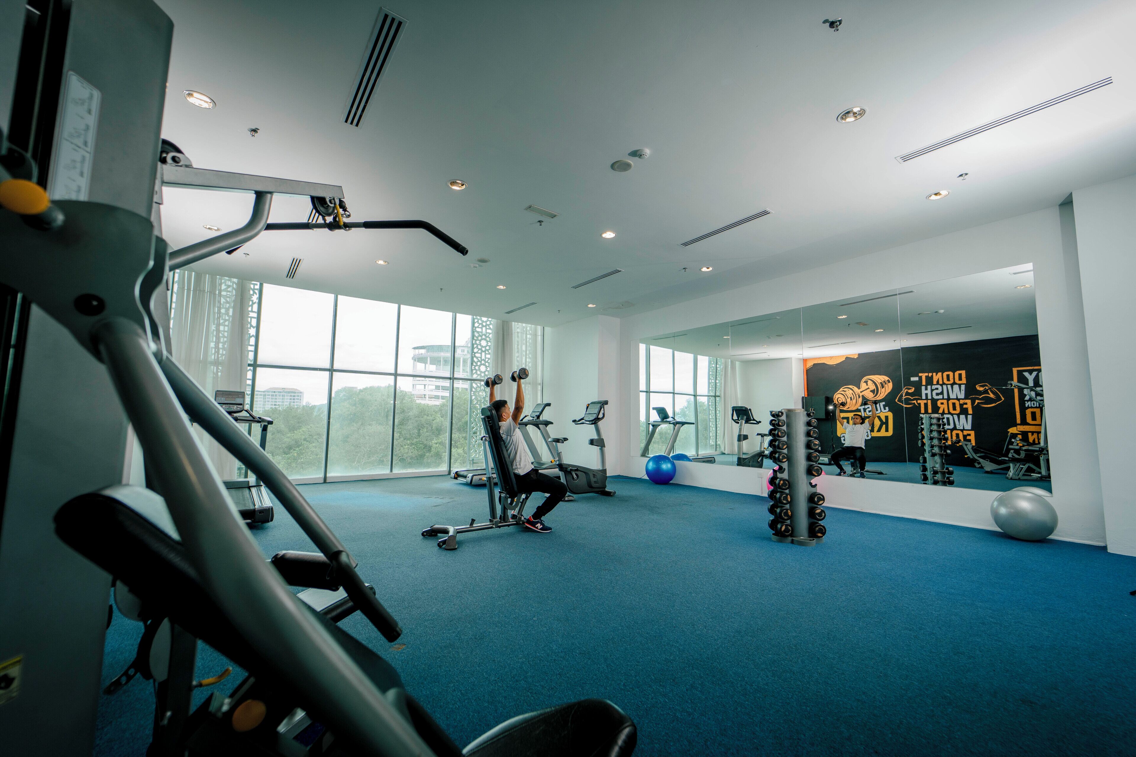A gym with exercise equipment, large windows, and a mirror wall.