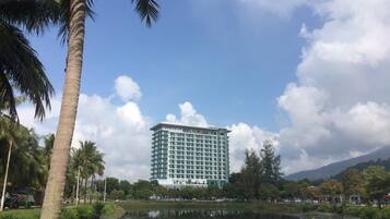 A high-rise hotel with a modern design, situated beside a calm lake with palm trees.