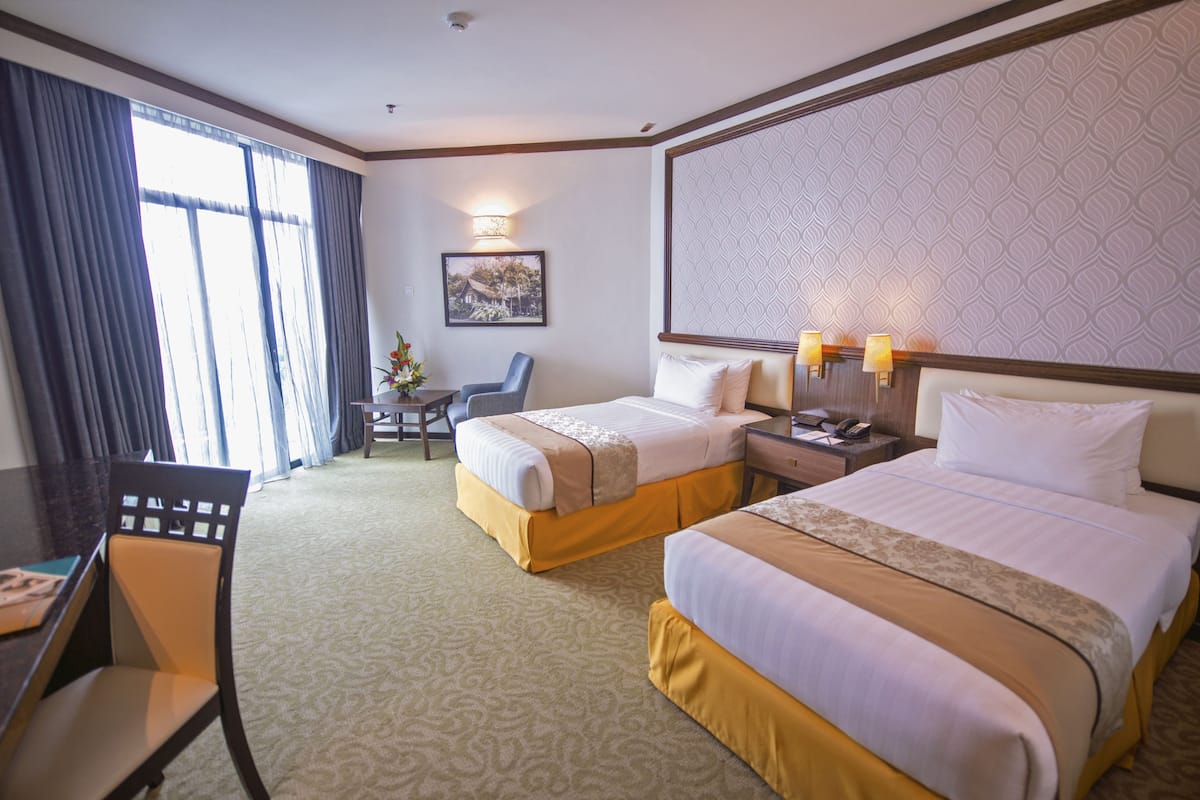 A hotel room with two beds, a desk, a chair, and a large window with curtains.