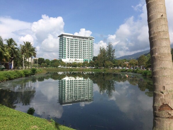 A high-rise hotel with a reflection in a calm body of water, surrounded by greenery and palm trees. - Adya Hotel Langkawi (Langkawi)