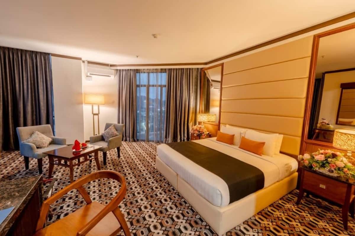 A hotel room with a large bed, a desk with a chair, a sofa, and a patterned carpet.