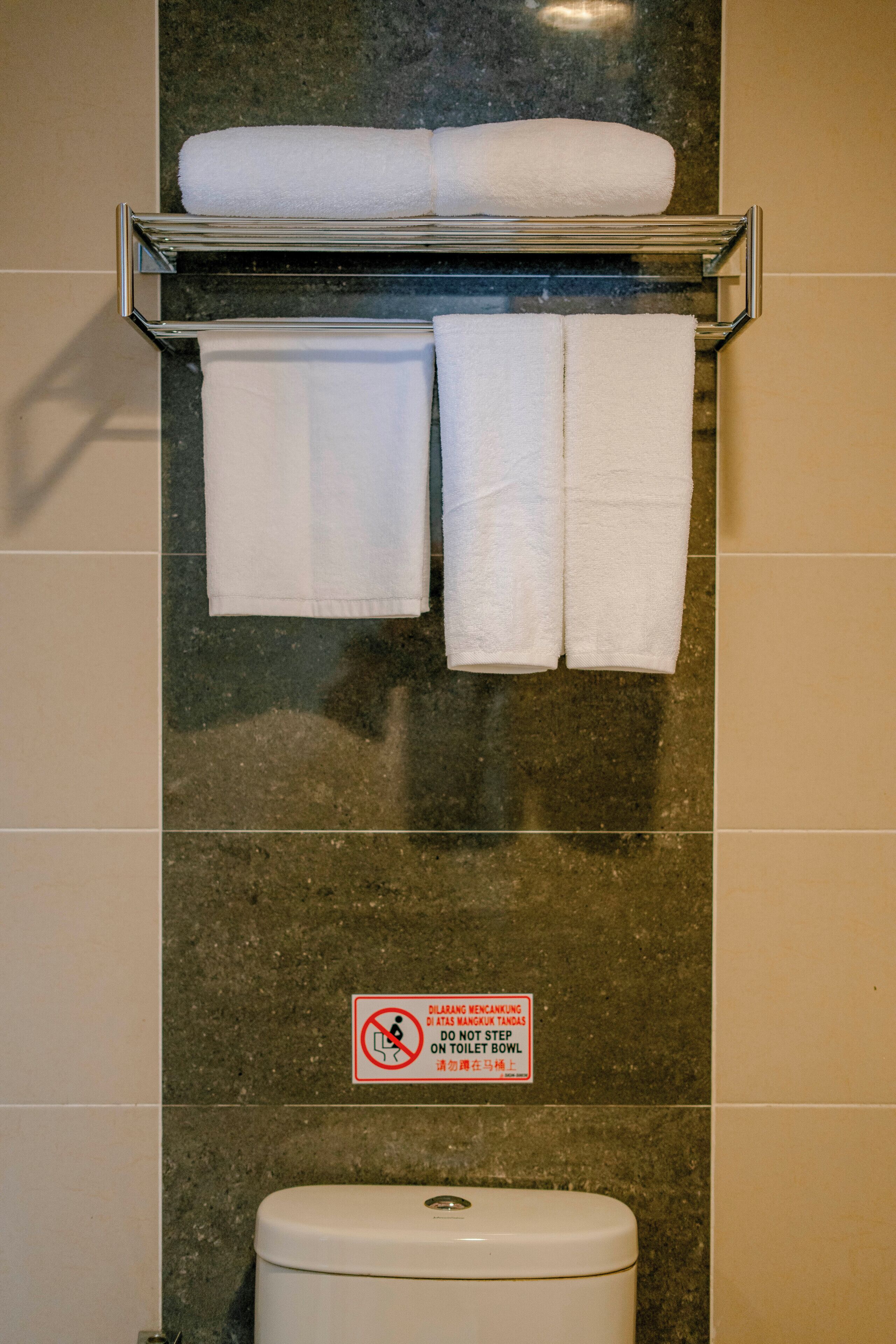 Une salle de bain comprenant des toilettes, un porte-serviettes avec deux serviettes et un panneau indiquant qu'il est interdit de poser les pieds sur la cuvette des toilettes.