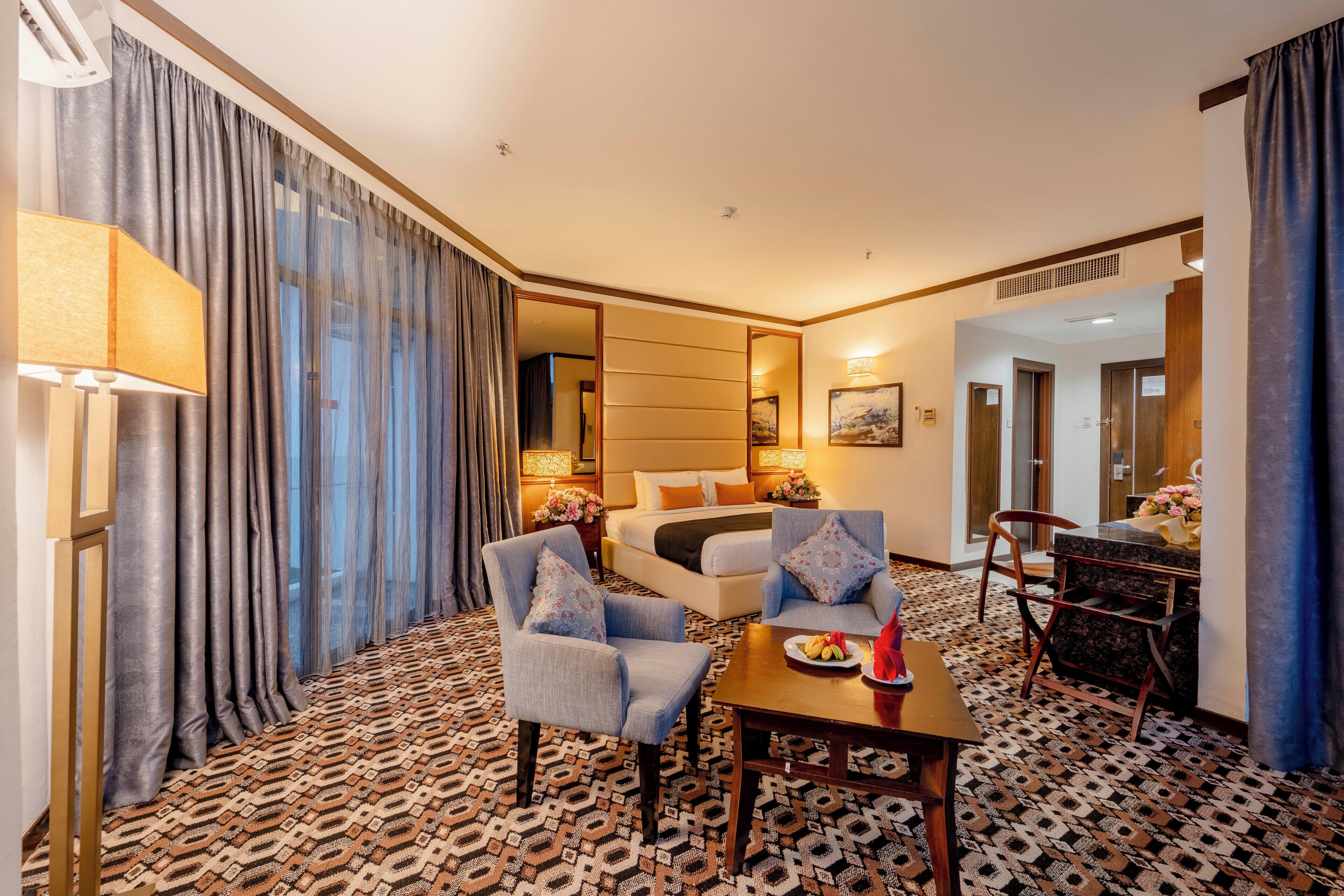 A hotel room with a bed, two armchairs, a table, a lamp, and a patterned carpet.