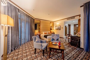 Una habitación de hotel con una cama, dos sillones, una mesa, una lámpara y una alfombra estampada.