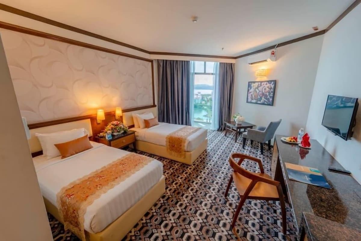 A hotel room with two beds, a desk, a chair, a TV, and a window with curtains.