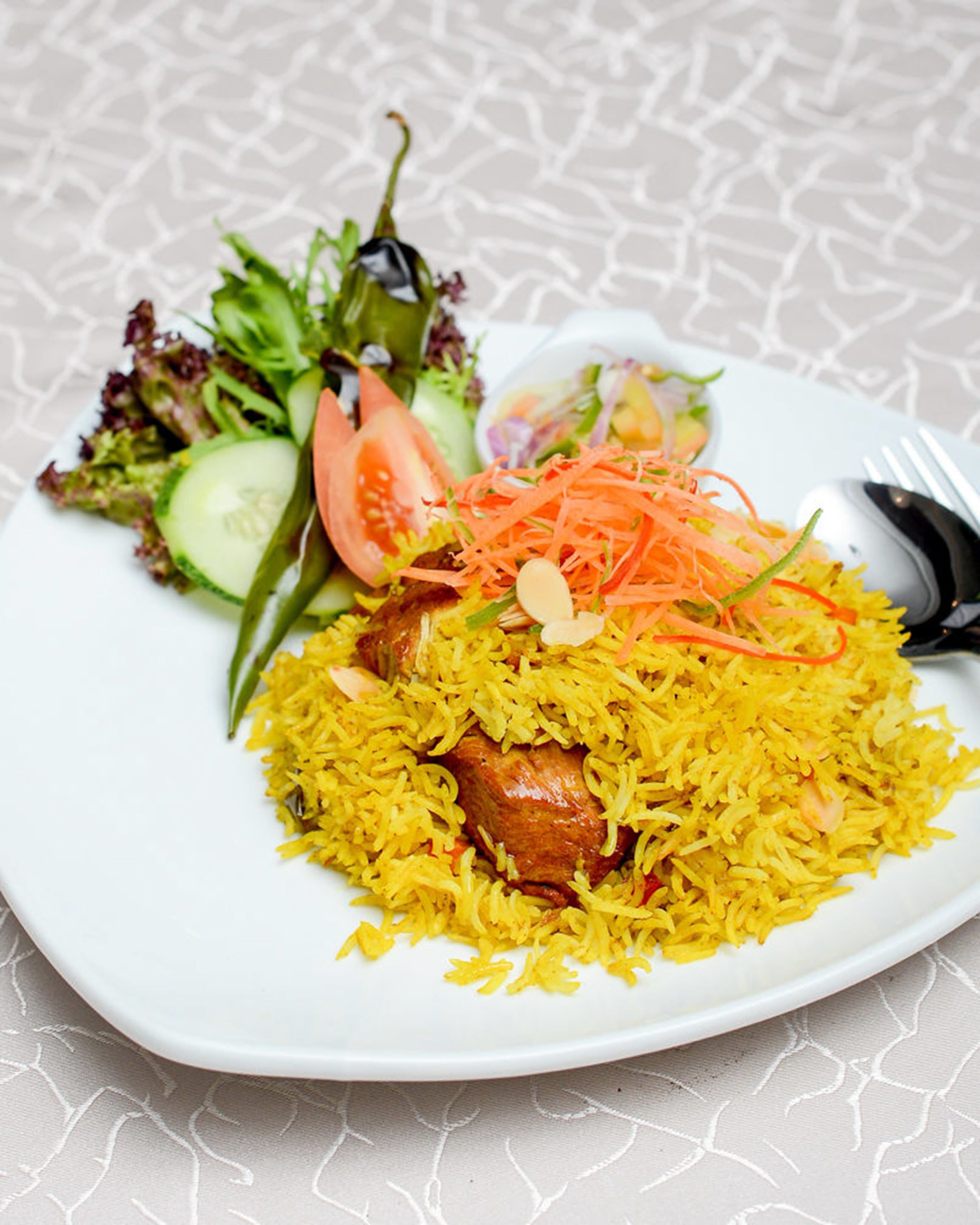 A plate of yellow rice with a piece of meat, accompanied by a side salad and a slice of tomato.