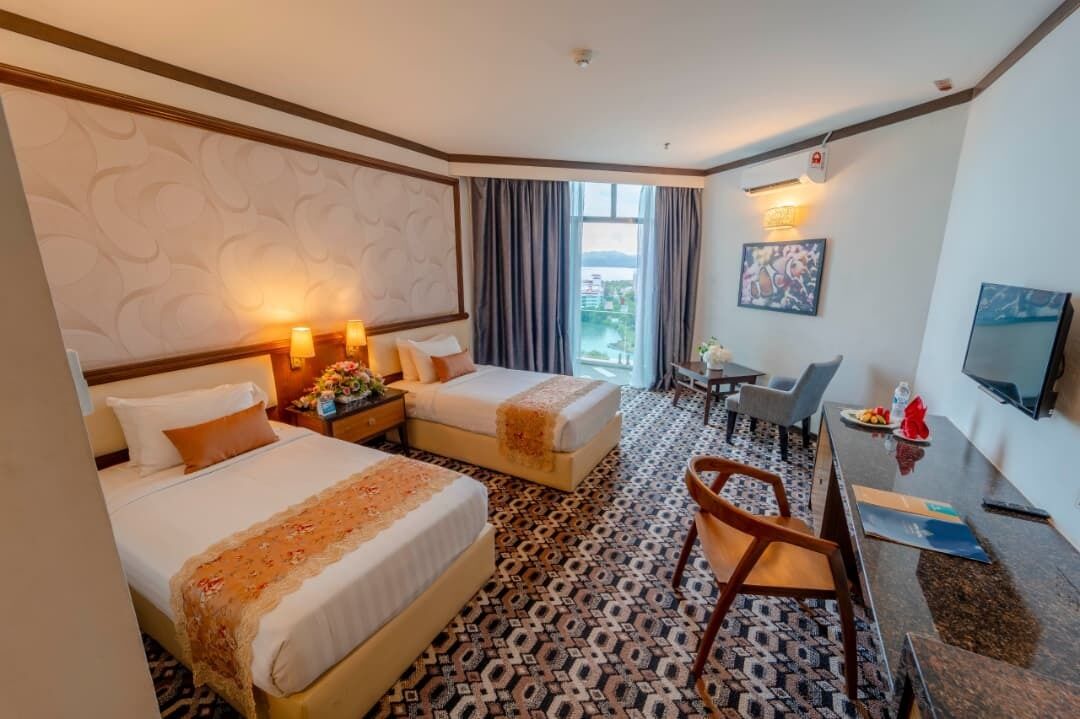 A hotel room with two beds, a desk, a chair, a TV, and a window with curtains.