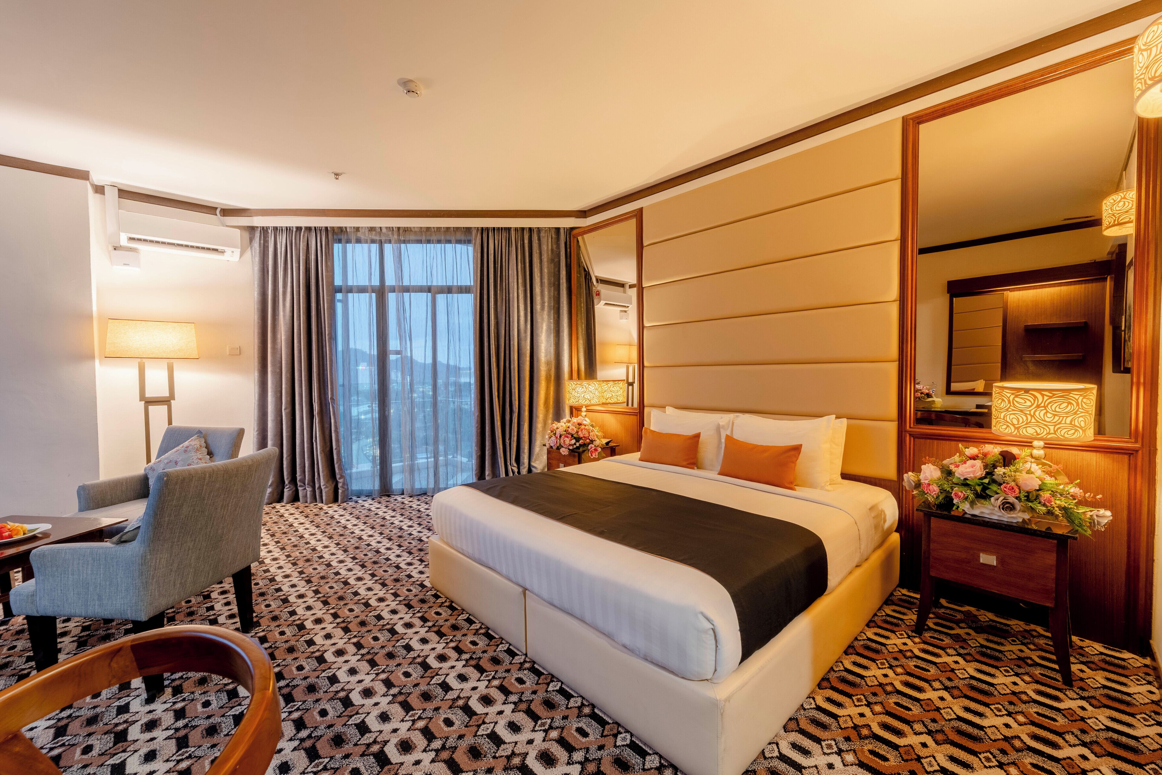A hotel room with a large bed, a desk, a chair, a nightstand, and a mirror.