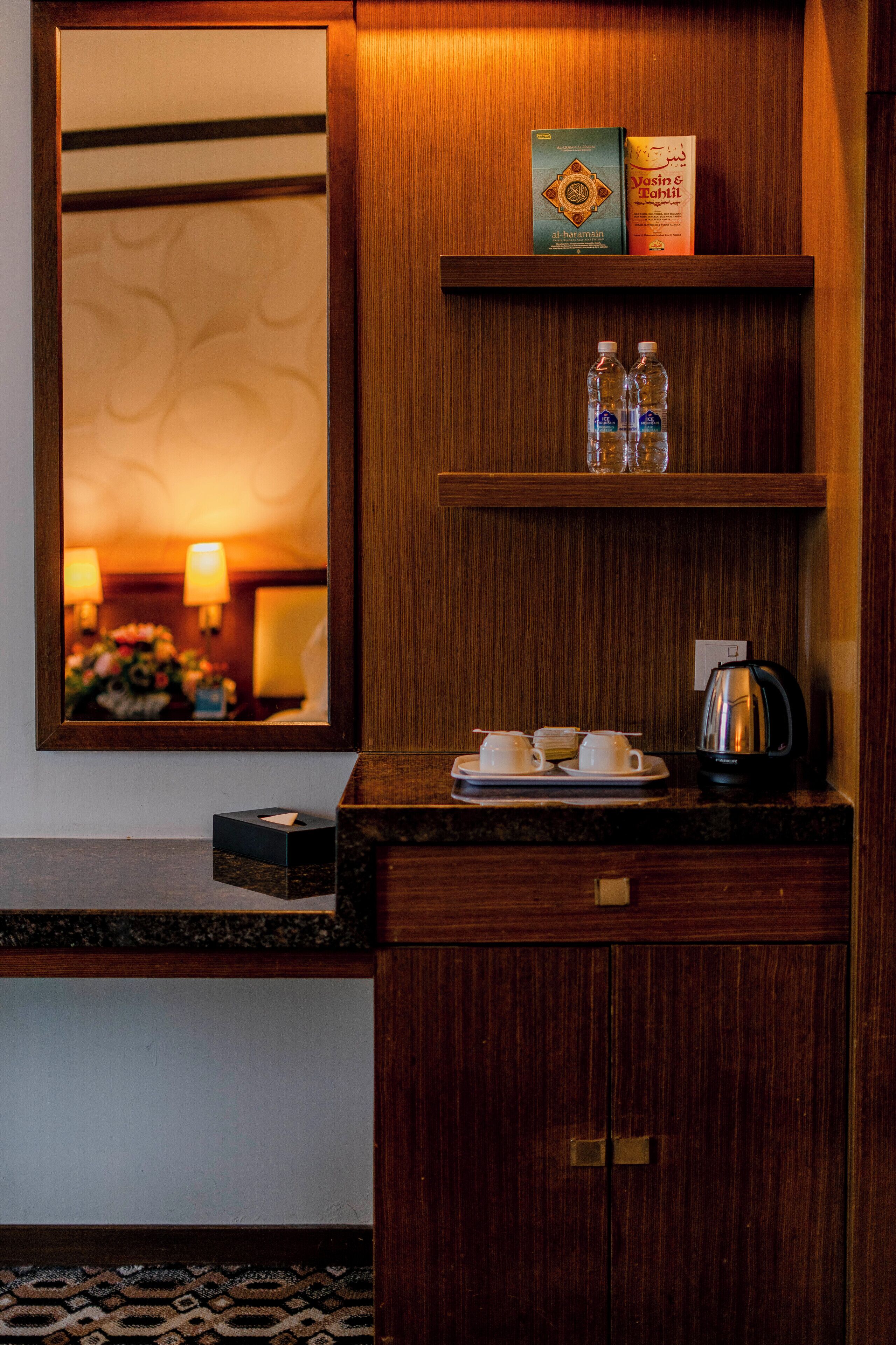 A hotel bathroom with a mirror, a shelf with toiletries, a coffee maker, and a tissue box.