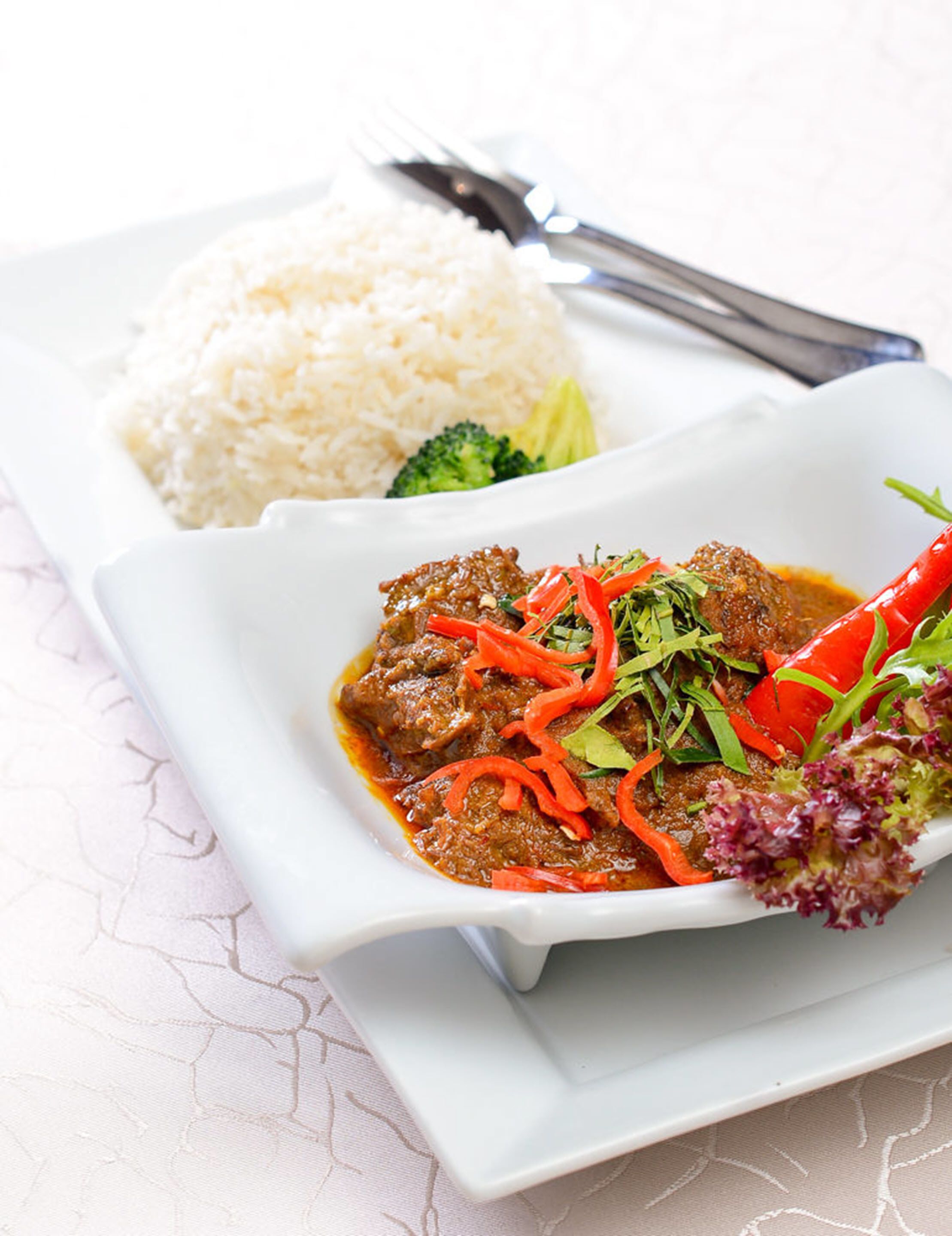 Un plato de comida con arroz y un guiso de carne adornado con pimientos rojos y vegetales verdes.