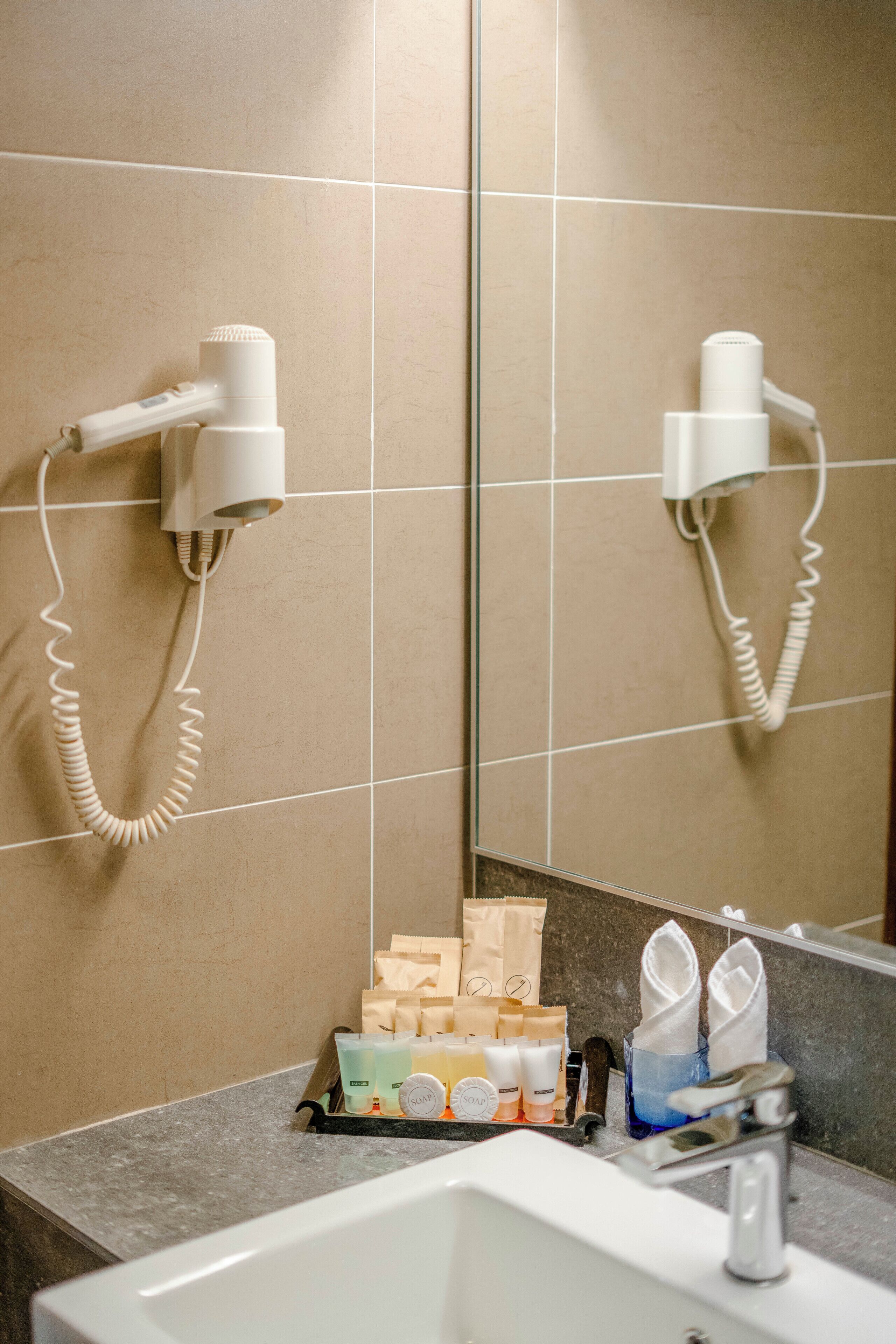 Une salle de bain équipée d’un lavabo, d’un miroir, de deux sèche-cheveux fixés au mur et d’une étagère contenant des articles de toilette.