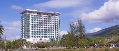 A multi-story hotel with a modern design, located near a body of water with a reflection.