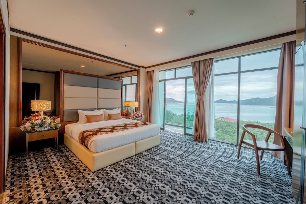 A hotel room with a large bed, a nightstand with a lamp, a chair, and a view of the mountains.