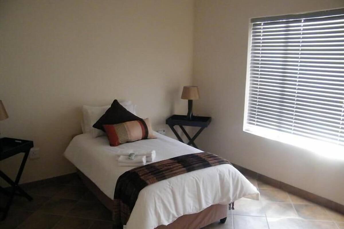 A hotel room with a bed, a nightstand, a lamp, and a window with blinds.