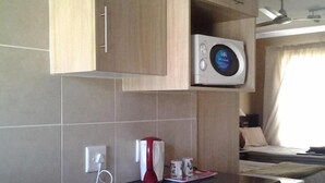 Eine kompakte Küche mit Holzausstattung, einer Mikrowelle, einer Kaffeemaschine und einem kleinen Kühlschrank.