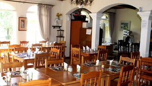 Ein Essbereich mit Holztischen und -stühlen, einer Chandelierleuchtre und Blick durch einen Rundbogen.