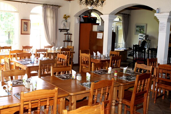 A dining area with wooden tables and chairs, a chandelier, and a view through an arched doorway.