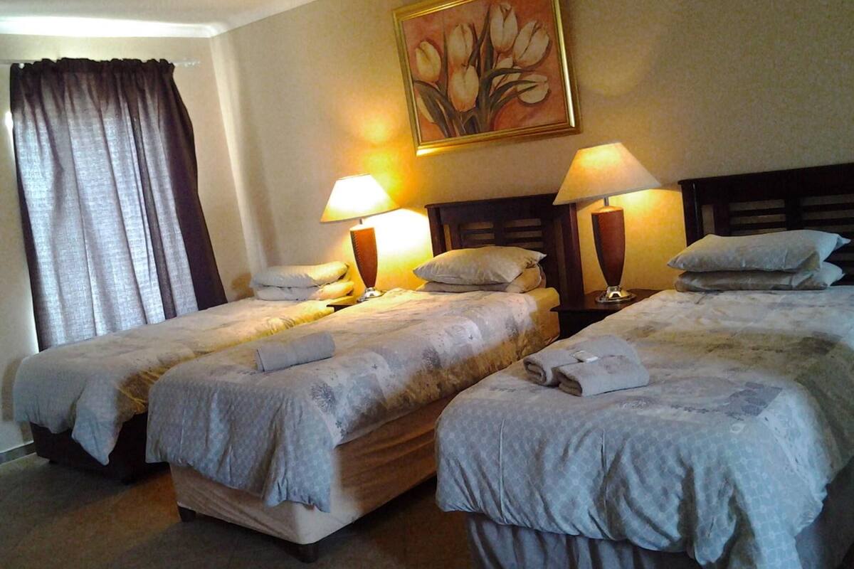 A hotel room with two beds, each with a lamp and pillows.