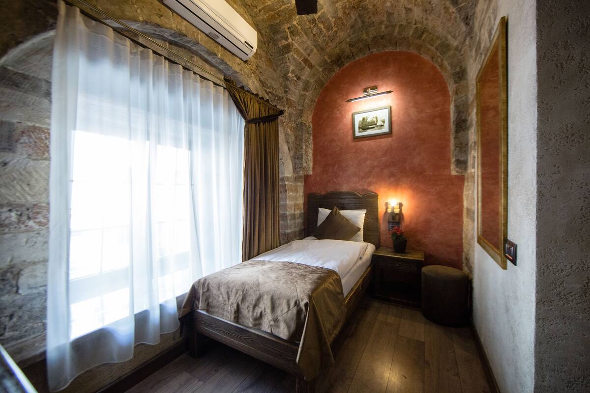 Ein Schlafzimmer mit Steinsturz, einem Bett mit hölzernem Kopfteil, einem Nachttisch und einem kleinen runden Tisch.