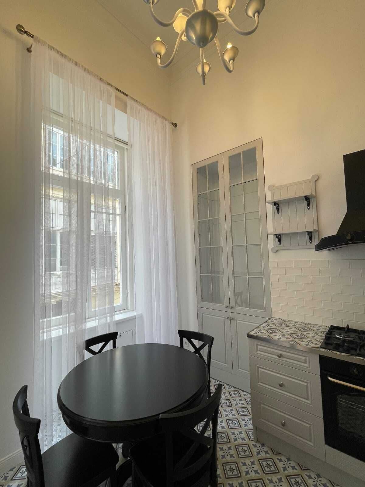 Una cocina con una mesa redonda, sillas, estufa y una ventana con cortinas.