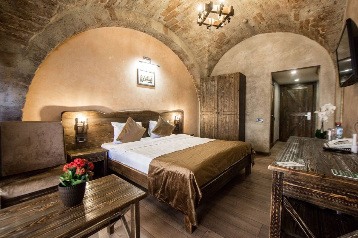Ein gemütliches Zimmer mit einem Bett, Holzmöbeln und einer Decke aus Steinbögen.