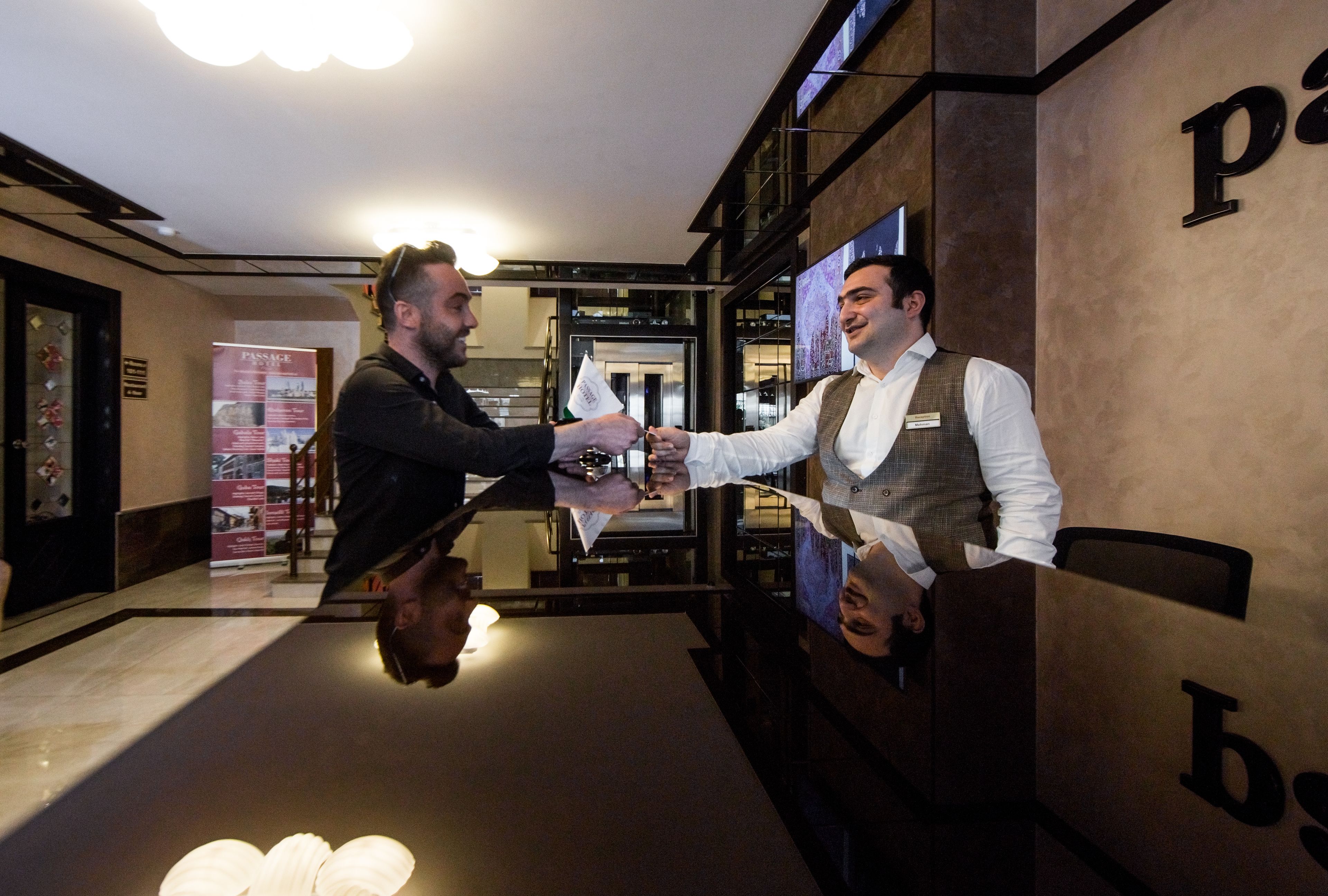 Deux personnes se serrent la main dans un hall d’entrée moderne, avec un comptoir d’accueil et une enseigne indiquant « Passage ».