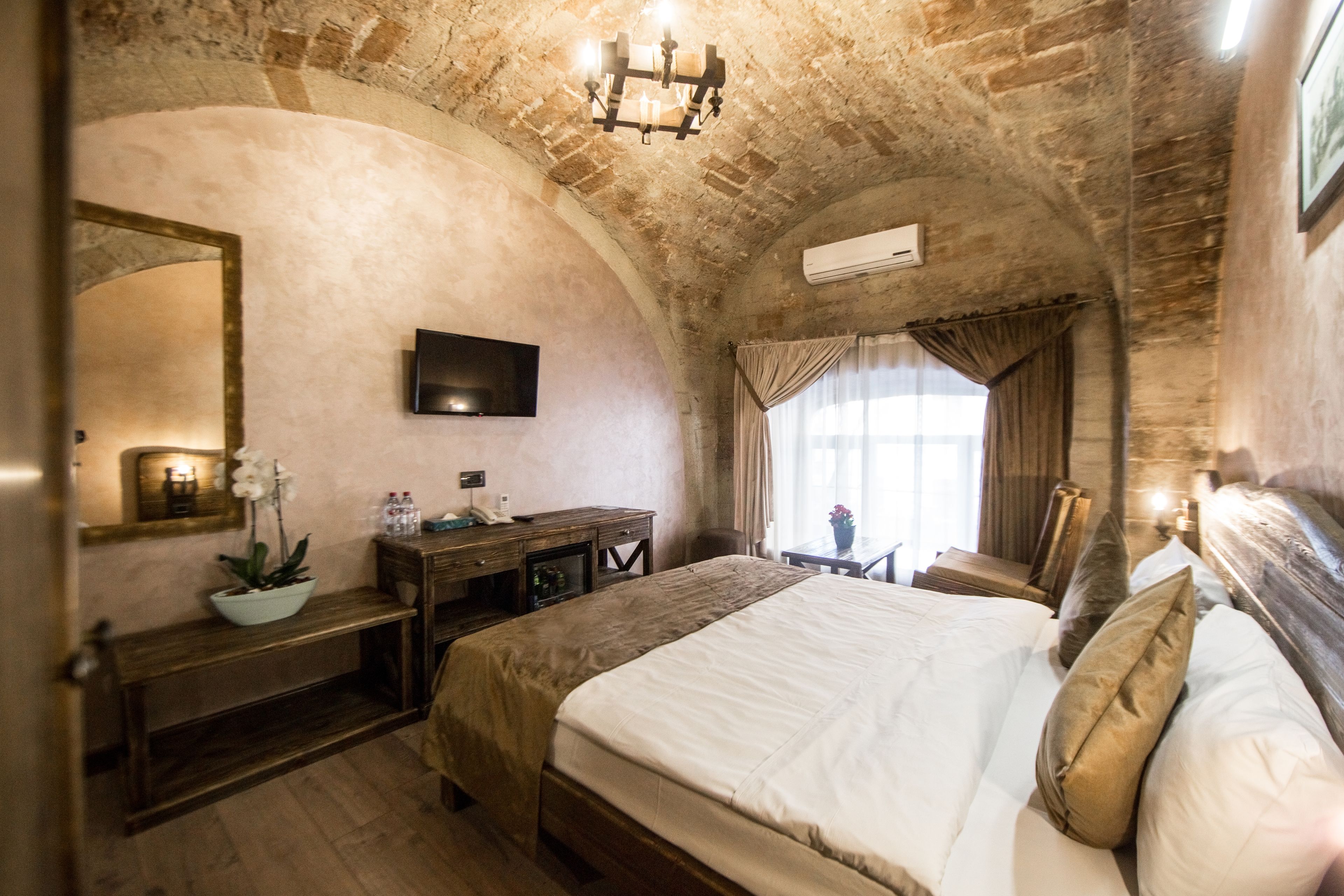 A bedroom with a large bed, a wooden dresser, a desk, a mirror, and a chandelier.