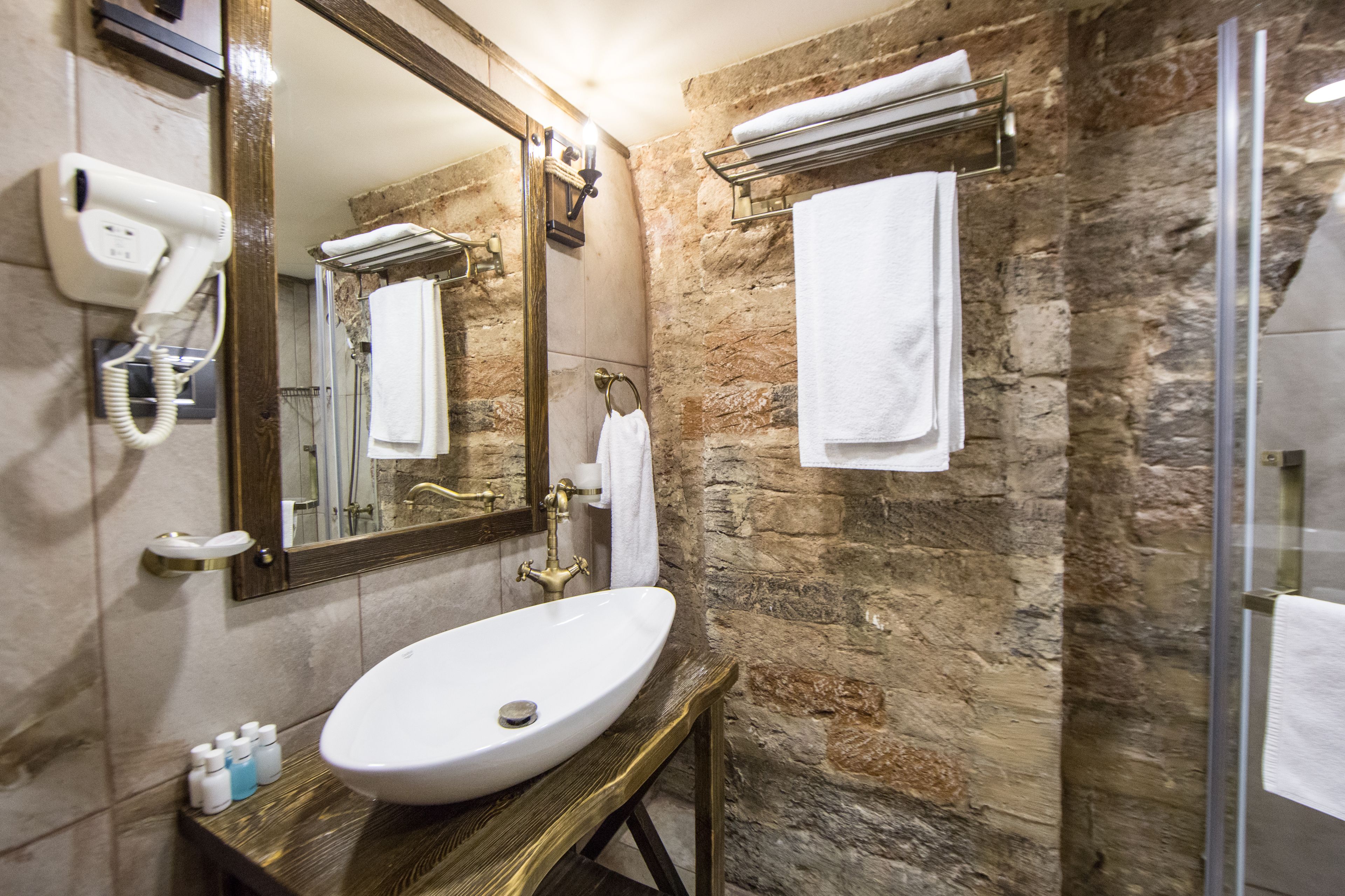 A bathroom with a stone wall, a sink, a mirror, a hairdryer, and a towel rack.