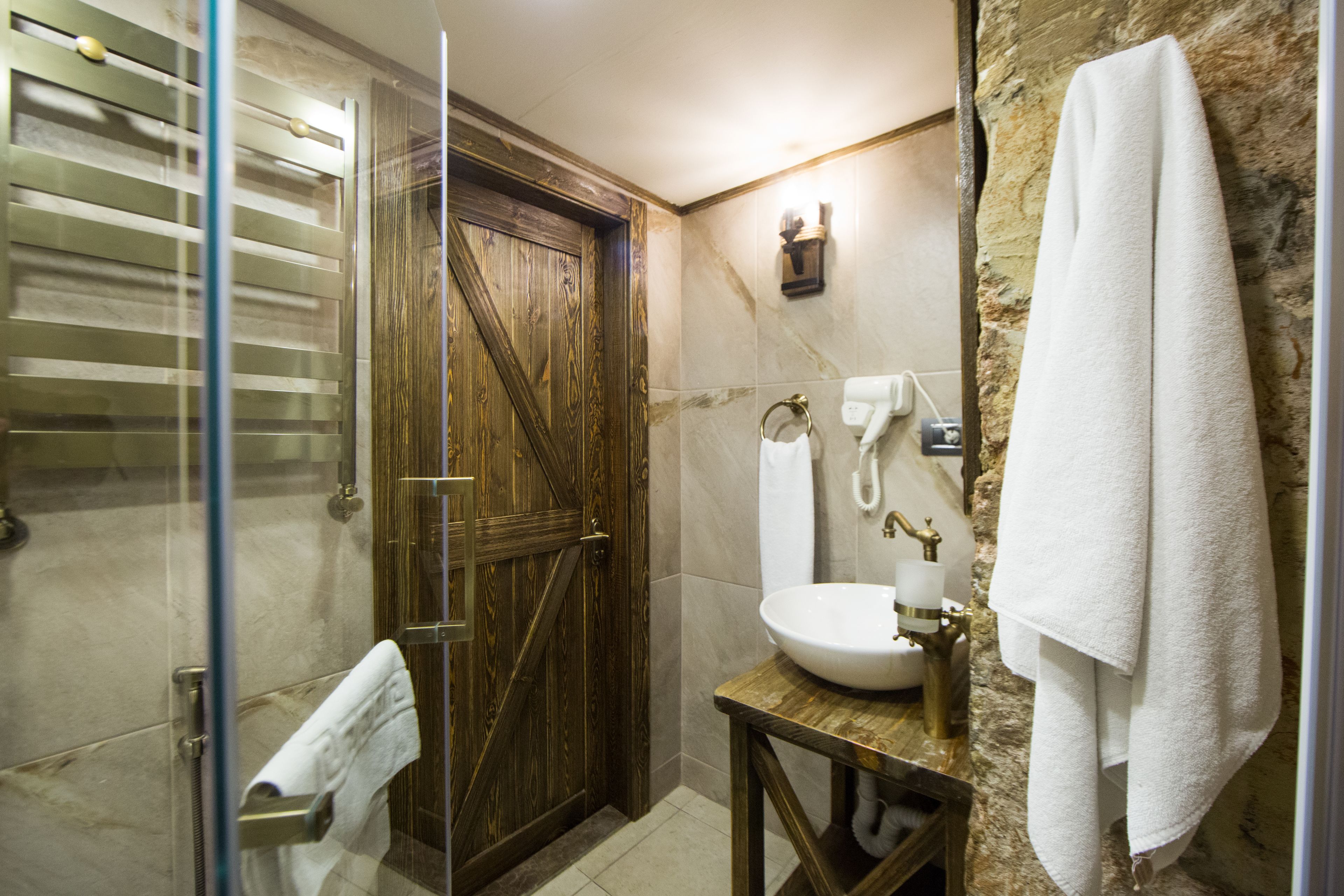 A bathroom with a wooden door, a glass shower enclosure, a sink with a marble countertop, and a towel hanging on the wall.