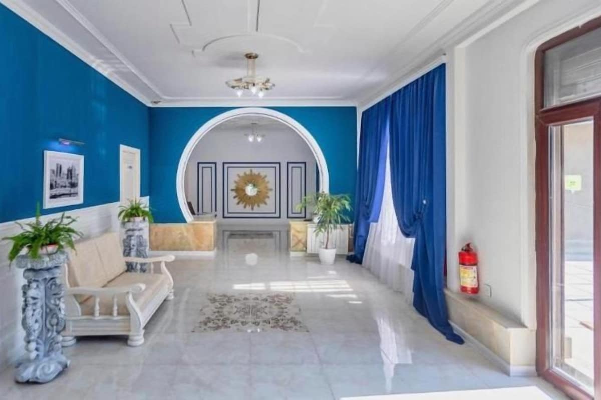 A hallway with a blue wall, a white bench, a sofa, and a chandelier.